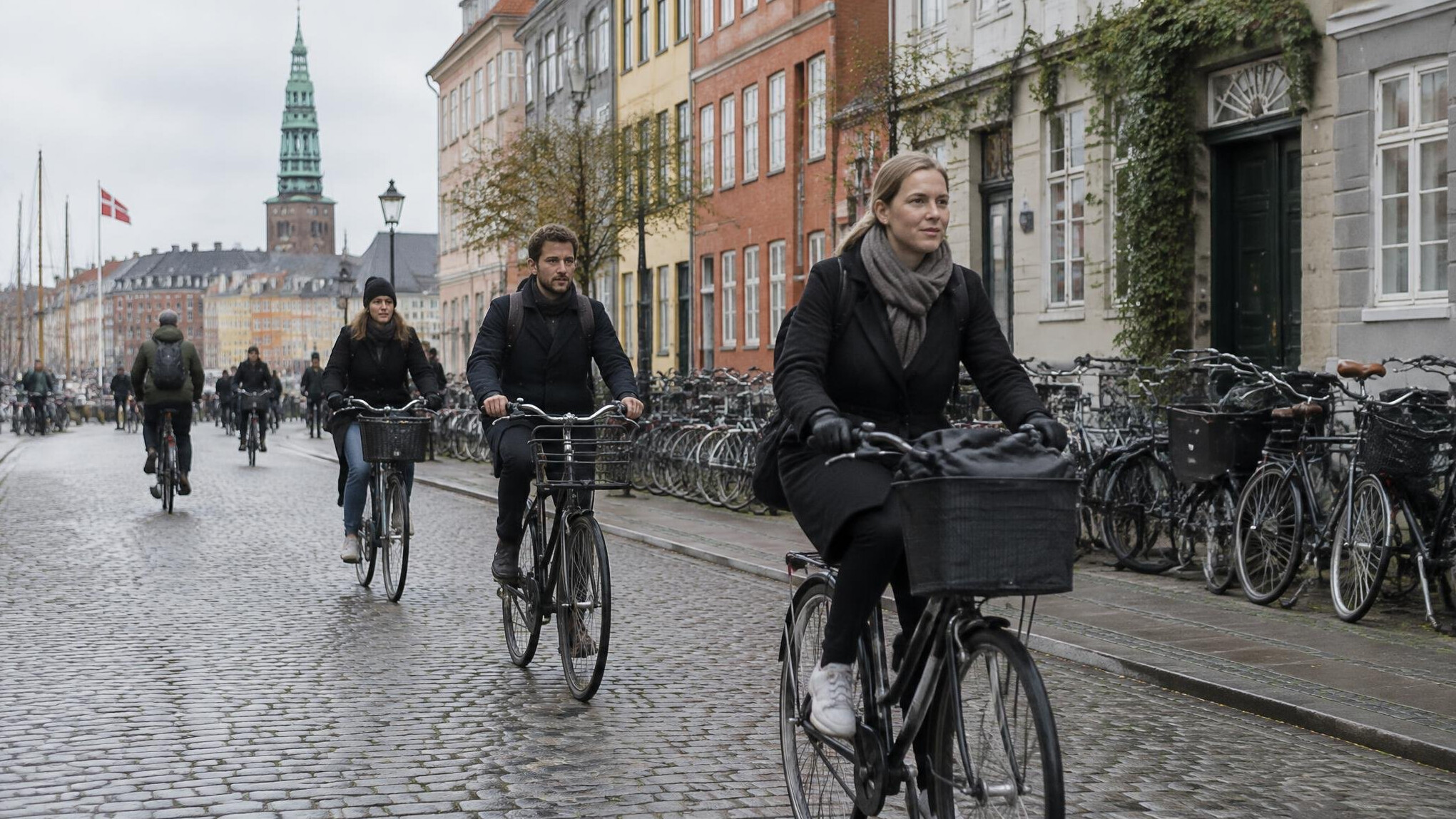 Cyclists riding through a Danish city street lined with bicycles