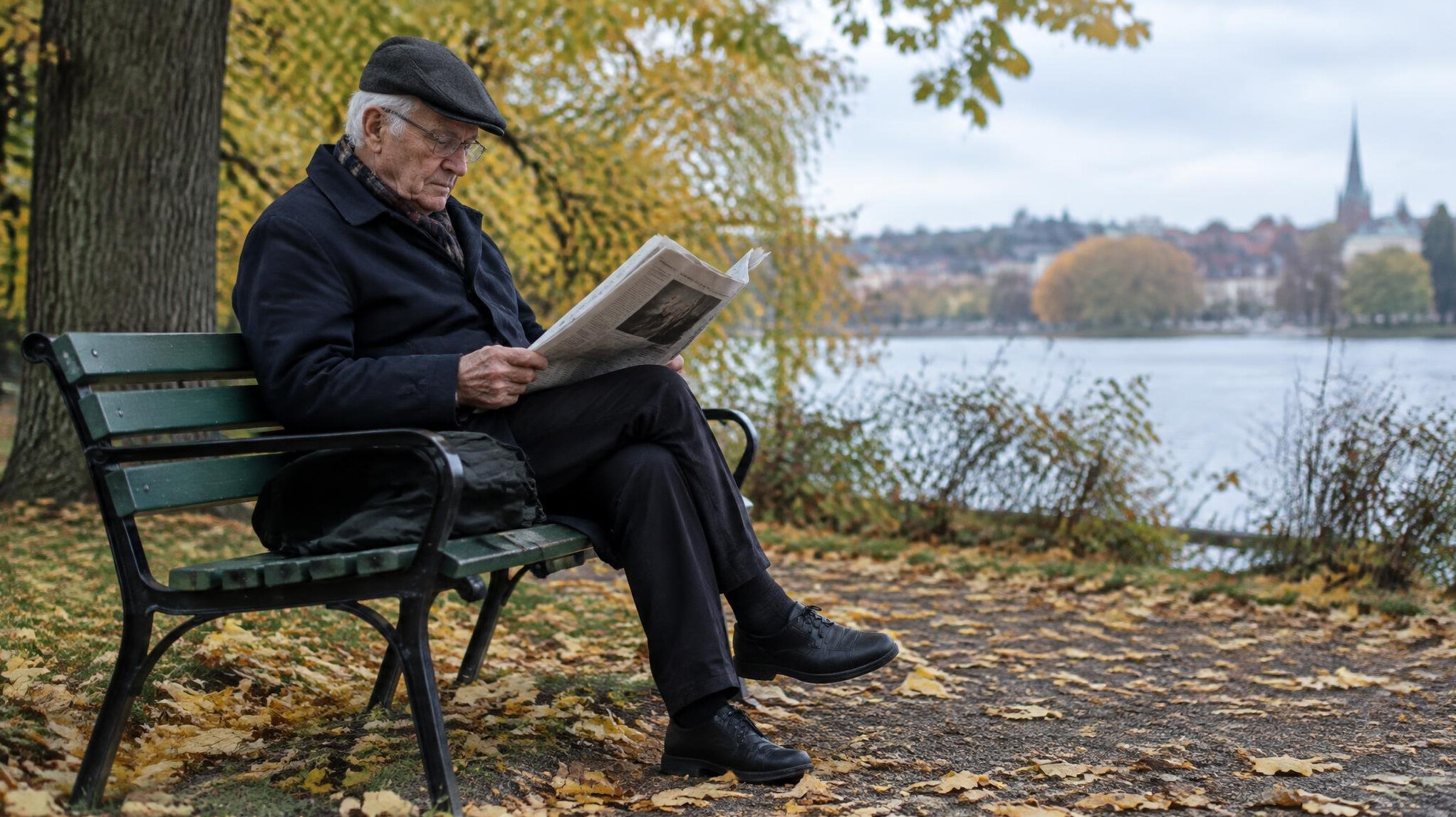 Elderly man sitting on a bench reading a newspaper in a park